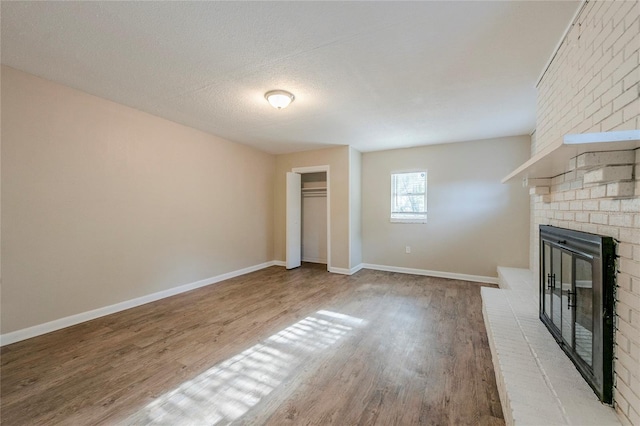 unfurnished living room with a brick fireplace, a textured ceiling, and hardwood / wood-style flooring