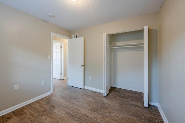 unfurnished bedroom with a textured ceiling, a closet, and wood-type flooring