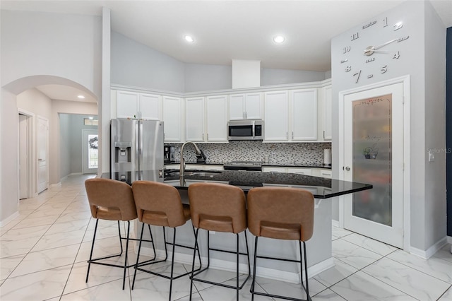 kitchen with stainless steel appliances, a kitchen island with sink, sink, high vaulted ceiling, and white cabinetry