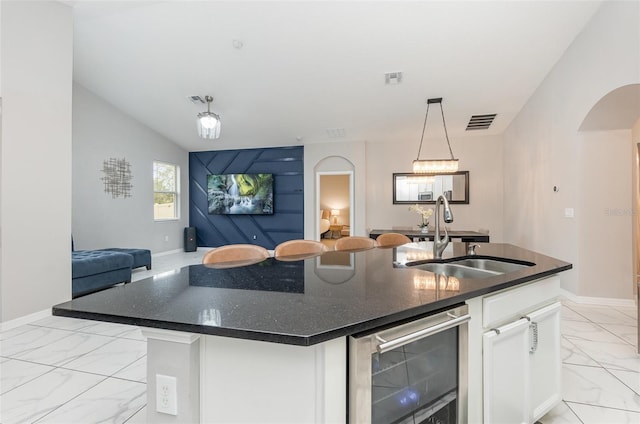 kitchen with white cabinetry, sink, wine cooler, an island with sink, and decorative light fixtures