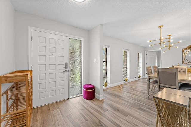 entrance foyer with light wood-type flooring, a textured ceiling, and a notable chandelier