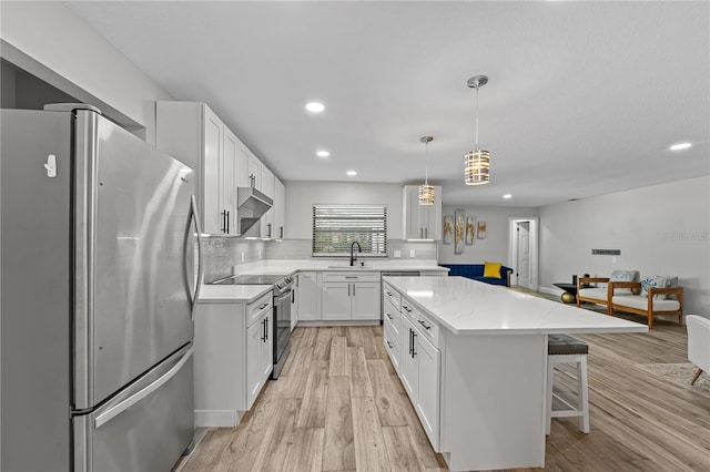 kitchen with appliances with stainless steel finishes, sink, a center island, white cabinetry, and hanging light fixtures