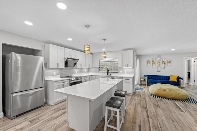 kitchen with appliances with stainless steel finishes, a kitchen island, sink, decorative light fixtures, and white cabinetry