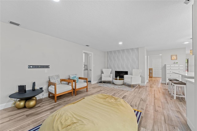 bedroom featuring a textured ceiling, a large fireplace, and light hardwood / wood-style floors