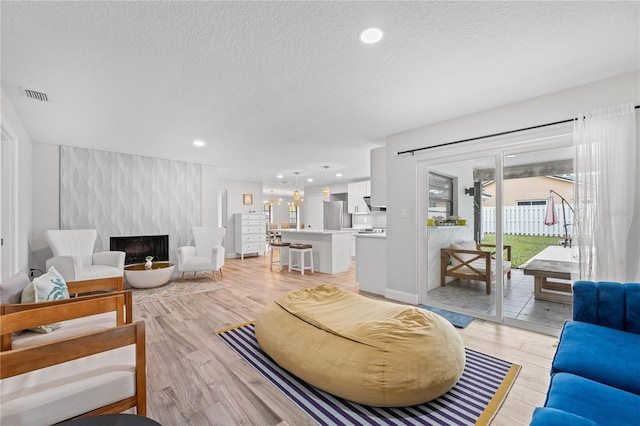 living room with a large fireplace, a textured ceiling, and light hardwood / wood-style flooring