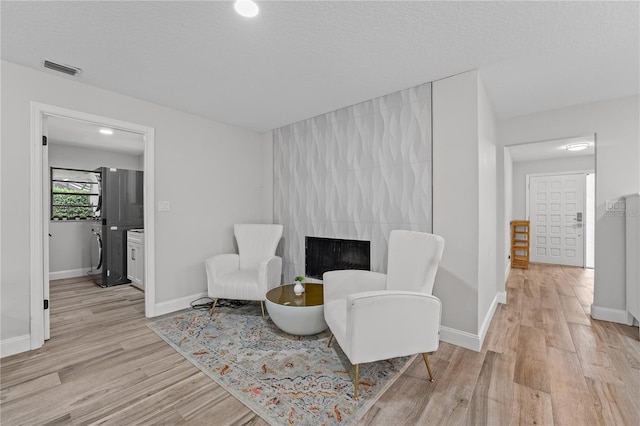 sitting room with a tiled fireplace, a textured ceiling, and light hardwood / wood-style flooring