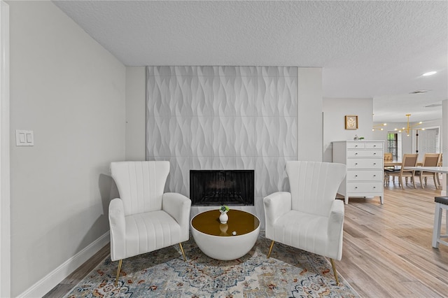 sitting room with a tile fireplace, a chandelier, a textured ceiling, and hardwood / wood-style flooring