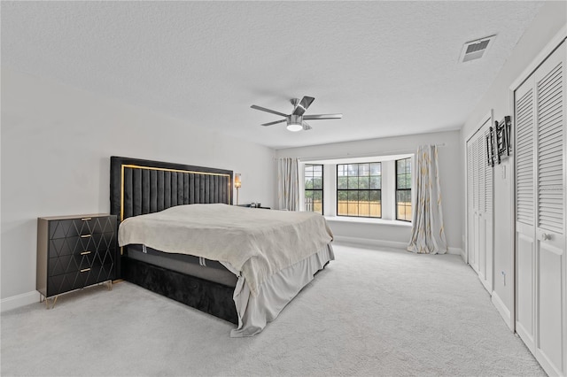 bedroom featuring light carpet, a textured ceiling, and ceiling fan