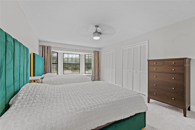 bedroom featuring a textured ceiling, ceiling fan, light carpet, and multiple closets