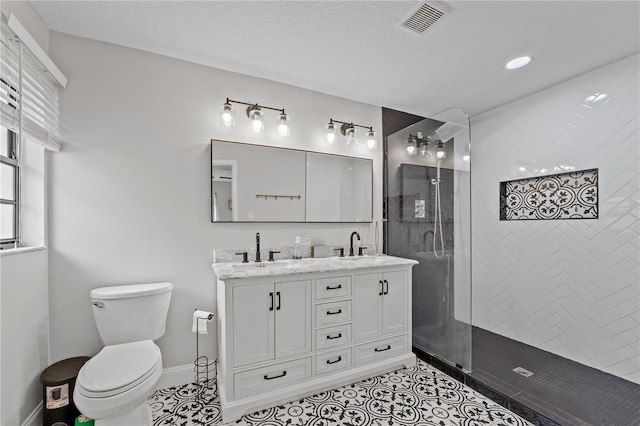 bathroom with a tile shower, tile patterned flooring, a textured ceiling, toilet, and vanity