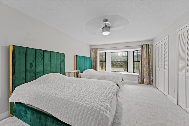 carpeted bedroom featuring multiple closets, ceiling fan, and a textured ceiling