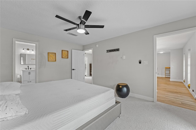 bedroom featuring light carpet, a textured ceiling, ceiling fan, sink, and connected bathroom