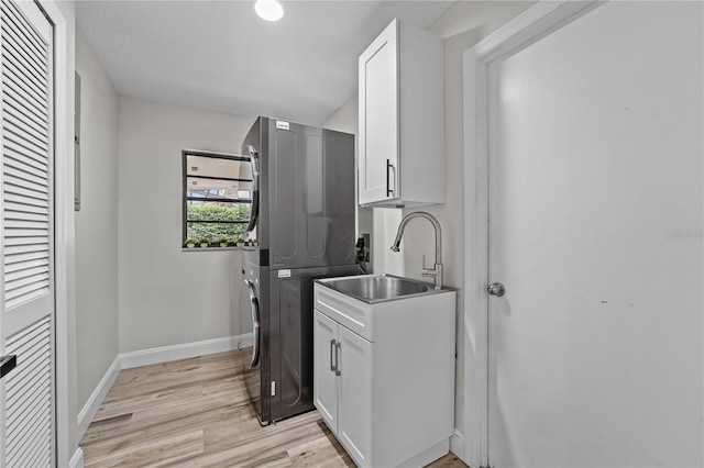 clothes washing area featuring cabinets, stacked washer and dryer, light hardwood / wood-style flooring, and sink