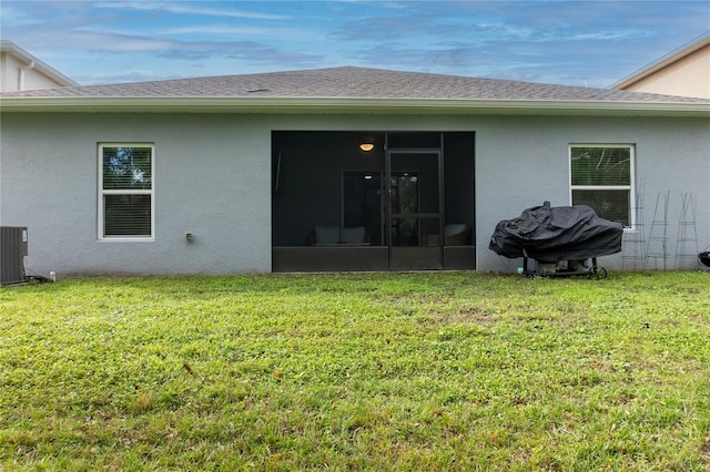 back of property featuring a sunroom, roof with shingles, stucco siding, and a yard