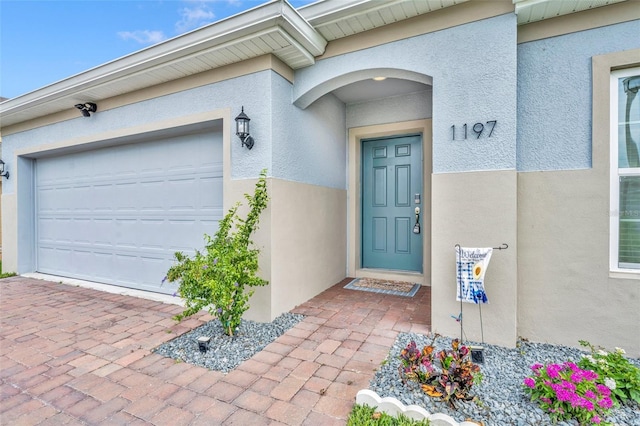 doorway to property featuring a garage, decorative driveway, and stucco siding