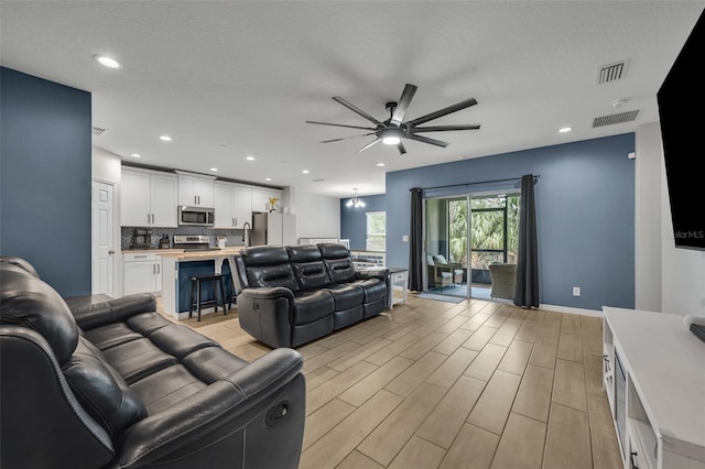 living room featuring light wood-type flooring, visible vents, recessed lighting, and ceiling fan with notable chandelier