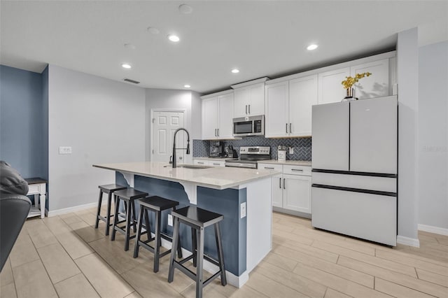 kitchen featuring light countertops, appliances with stainless steel finishes, white cabinetry, an island with sink, and a kitchen breakfast bar