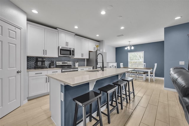 kitchen featuring appliances with stainless steel finishes, a sink, a kitchen island with sink, and white cabinetry