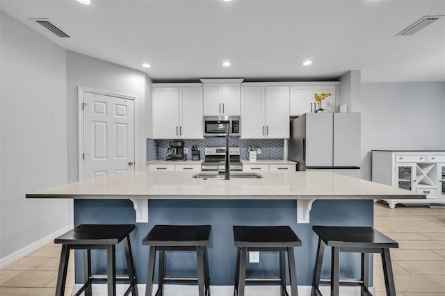 kitchen with visible vents, appliances with stainless steel finishes, a large island with sink, and white cabinetry