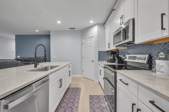 kitchen with light countertops, backsplash, appliances with stainless steel finishes, white cabinets, and a sink