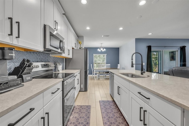 kitchen featuring white cabinets, appliances with stainless steel finishes, light countertops, pendant lighting, and a sink