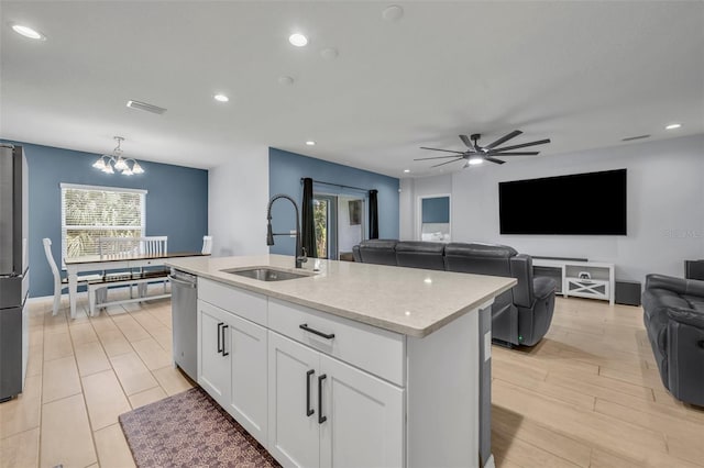 kitchen featuring a kitchen island with sink, a sink, white cabinets, open floor plan, and pendant lighting