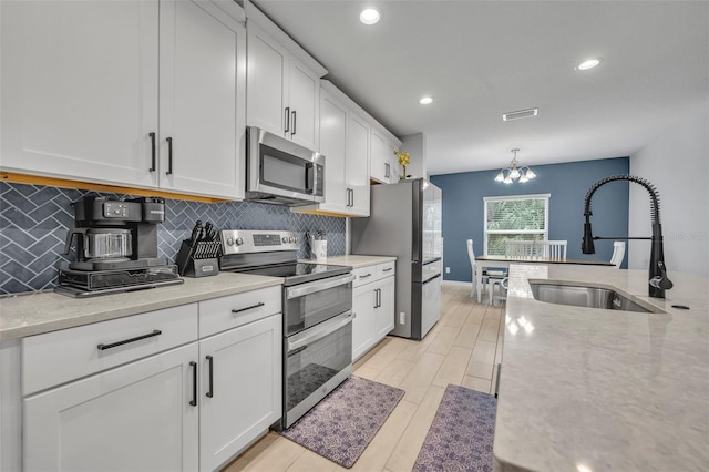 kitchen with pendant lighting, stainless steel appliances, decorative backsplash, white cabinetry, and a sink