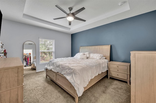 bedroom featuring baseboards, light colored carpet, ceiling fan, a spacious closet, and a tray ceiling