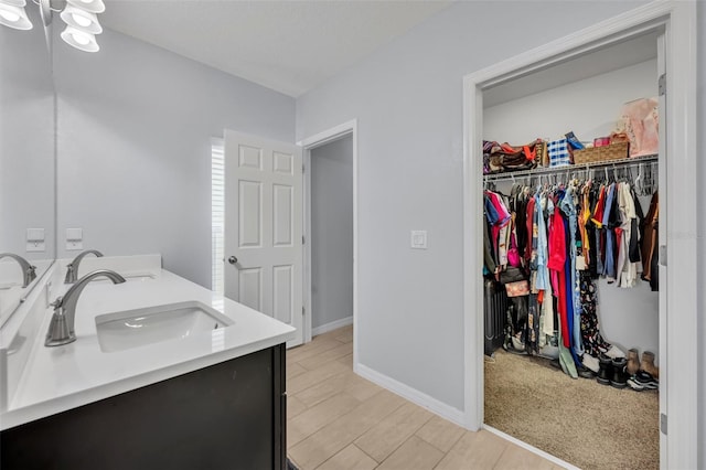 bathroom with double vanity, baseboards, wood finished floors, a walk in closet, and a sink