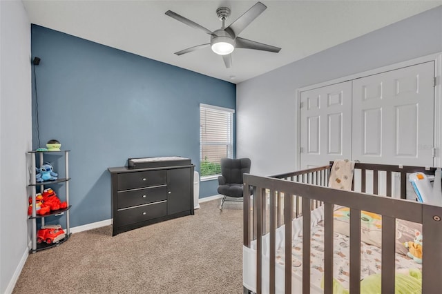 carpeted bedroom with a ceiling fan, a nursery area, a closet, and baseboards