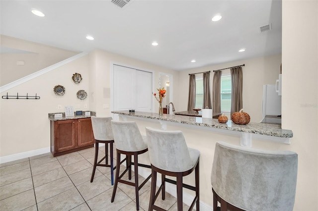 kitchen with kitchen peninsula, light stone counters, a breakfast bar area, and light tile patterned flooring