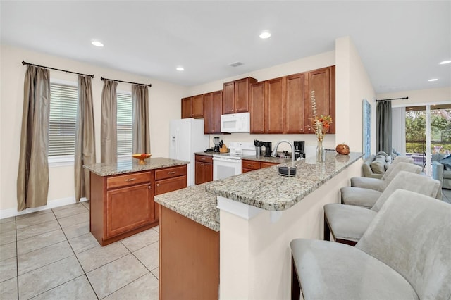 kitchen with white appliances, light tile patterned floors, light stone countertops, kitchen peninsula, and a breakfast bar area