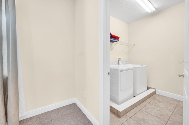 clothes washing area with light tile patterned floors, washer and dryer, and a textured ceiling