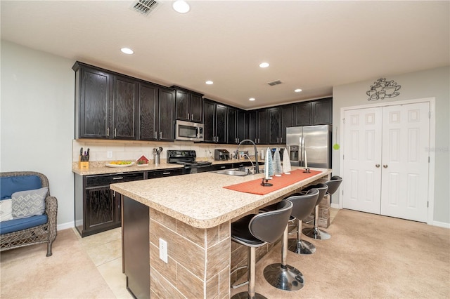 kitchen with sink, a kitchen breakfast bar, a kitchen island with sink, light tile patterned flooring, and appliances with stainless steel finishes