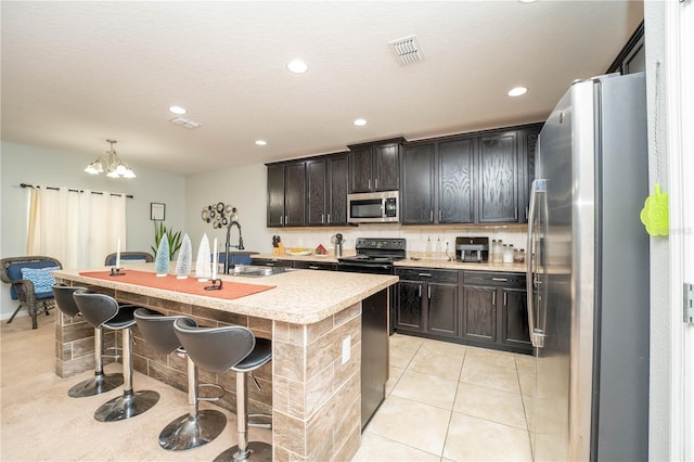 kitchen with sink, an inviting chandelier, a kitchen bar, a kitchen island with sink, and appliances with stainless steel finishes