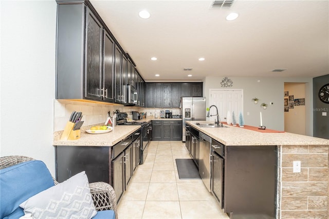 kitchen with appliances with stainless steel finishes, backsplash, a kitchen island with sink, sink, and light tile patterned floors