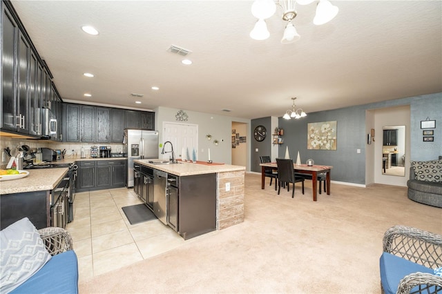 kitchen with sink, hanging light fixtures, a chandelier, a center island with sink, and appliances with stainless steel finishes