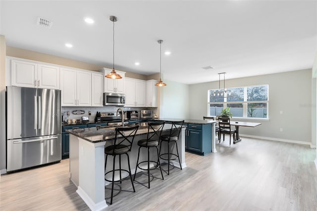 kitchen featuring stainless steel appliances, blue cabinetry, pendant lighting, white cabinets, and an island with sink