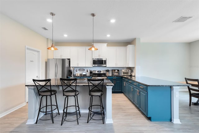 kitchen featuring a center island, white cabinets, blue cabinets, appliances with stainless steel finishes, and decorative light fixtures