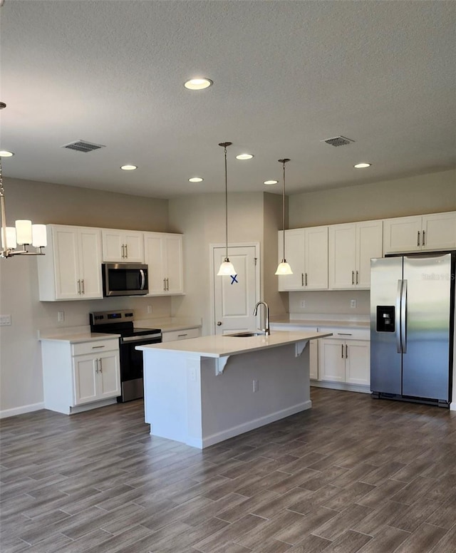 kitchen featuring stainless steel appliances, dark hardwood / wood-style floors, pendant lighting, a kitchen island with sink, and white cabinets