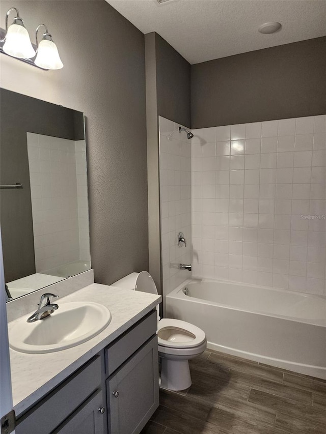 full bathroom featuring vanity, a textured ceiling,  shower combination, hardwood / wood-style floors, and toilet