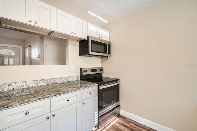 kitchen featuring dark stone counters, white cabinetry, appliances with stainless steel finishes, and a textured ceiling