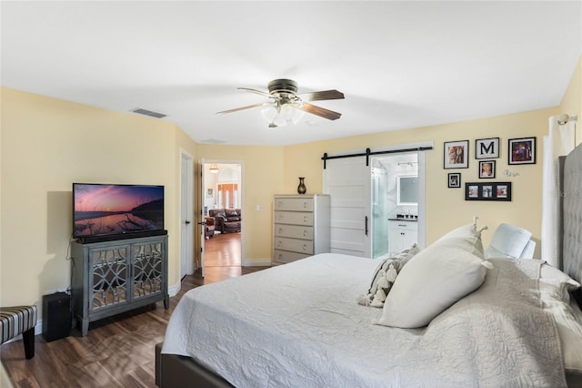 bedroom featuring dark hardwood / wood-style flooring, a barn door, ceiling fan, and connected bathroom