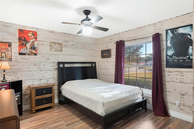 bedroom with wood-type flooring, ceiling fan, and wooden walls