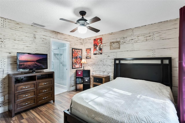 bedroom featuring ceiling fan, dark hardwood / wood-style flooring, wood walls, ensuite bathroom, and a textured ceiling