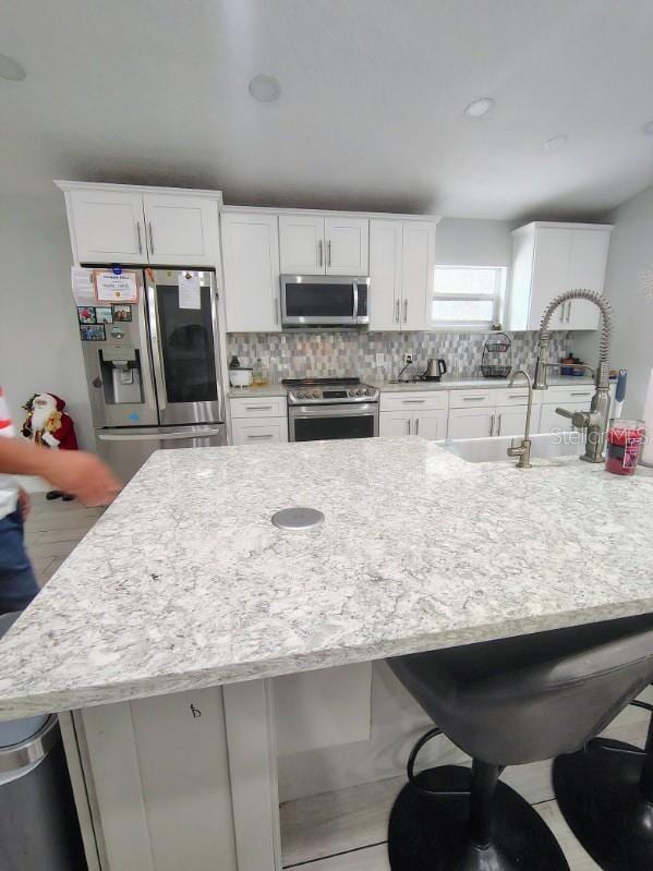 kitchen with sink, tasteful backsplash, a breakfast bar area, white cabinets, and appliances with stainless steel finishes