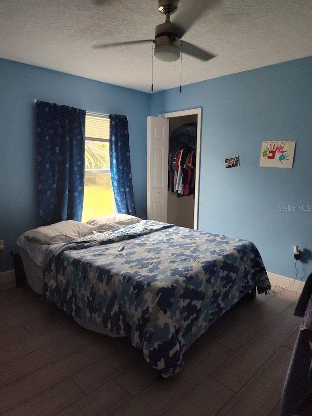 bedroom with ceiling fan, dark hardwood / wood-style floors, a textured ceiling, and a closet