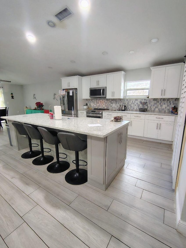 kitchen with white cabinets, a kitchen bar, a kitchen island with sink, and appliances with stainless steel finishes