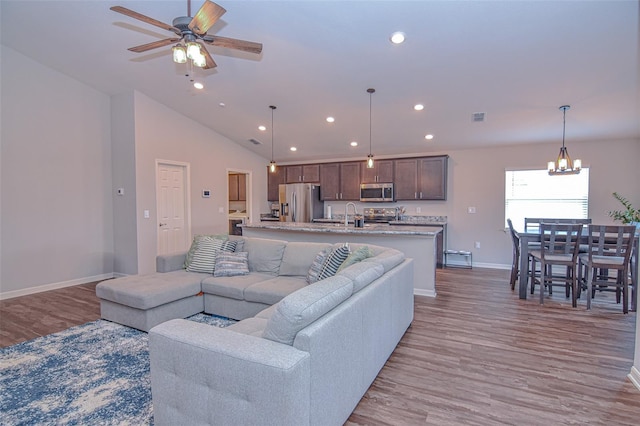 living room with ceiling fan with notable chandelier, light wood-type flooring, sink, and lofted ceiling