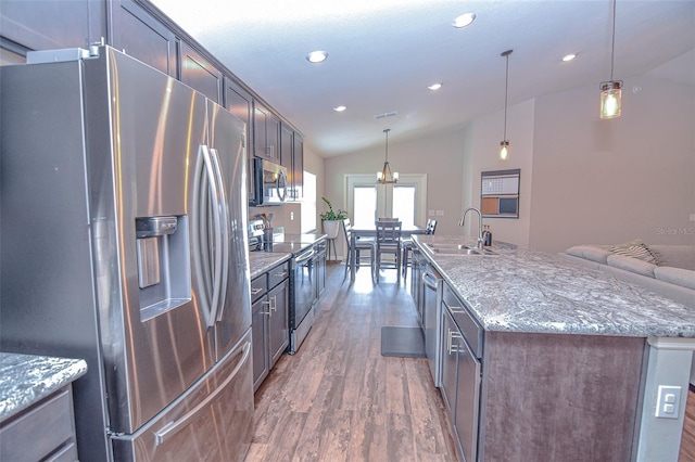 kitchen with sink, hanging light fixtures, vaulted ceiling, an island with sink, and stainless steel appliances